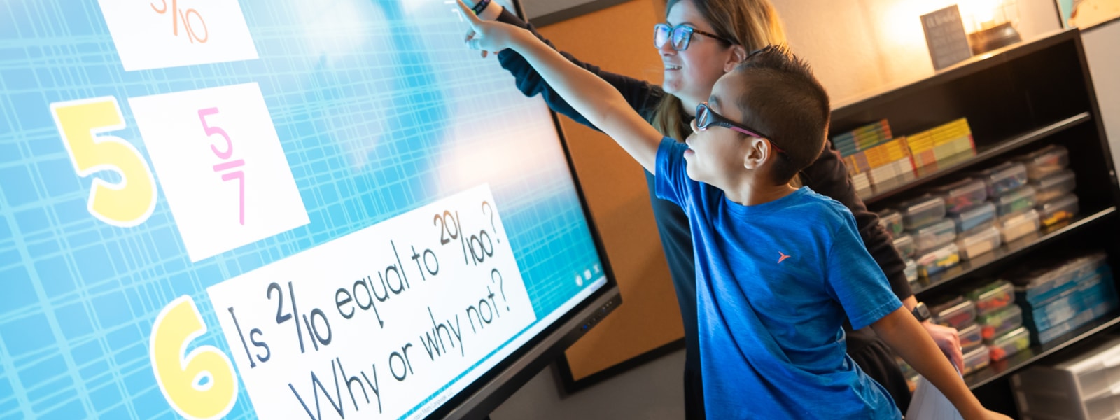 A teacher helping a student with math on a smart board.