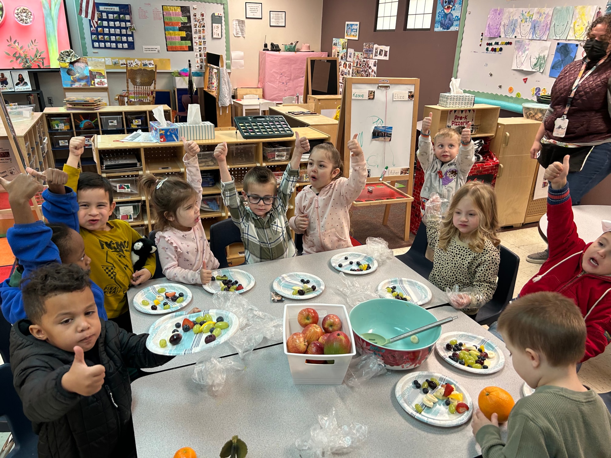 Preschool Students eating fruit and giving a thumbs up sign.