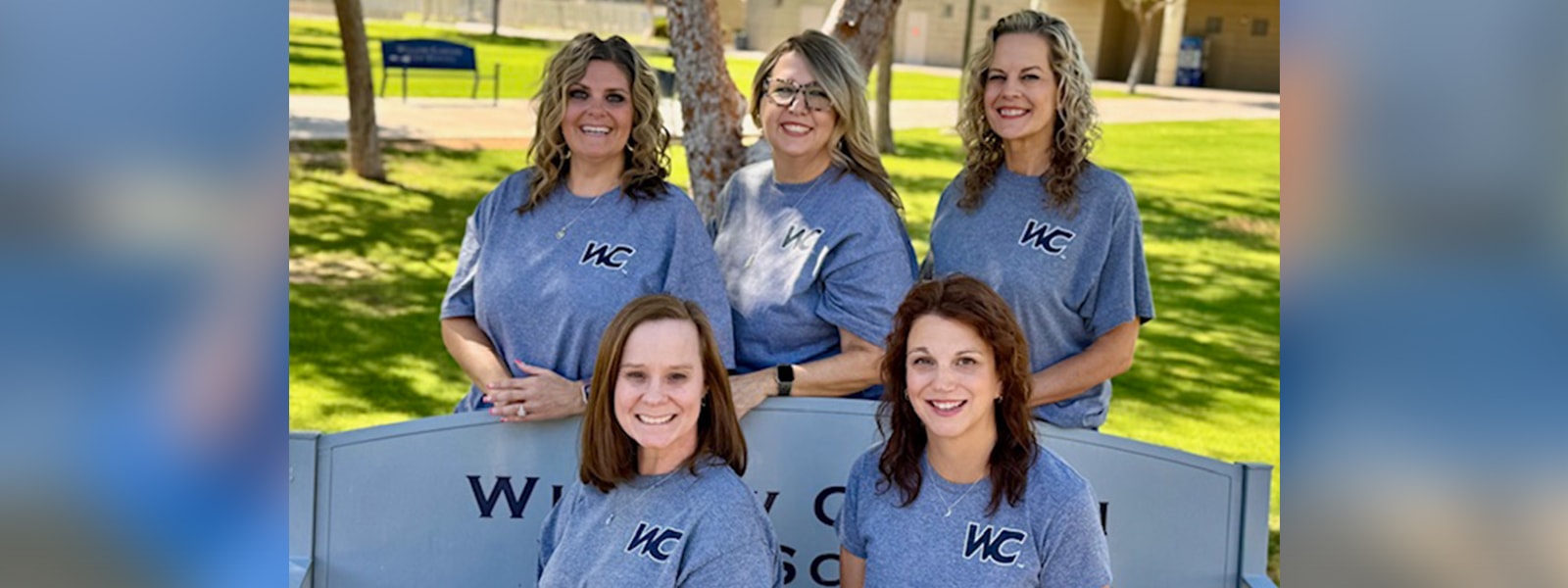 5 counselors 2 sitting on a bench and 3 standing with grass and trees in the background